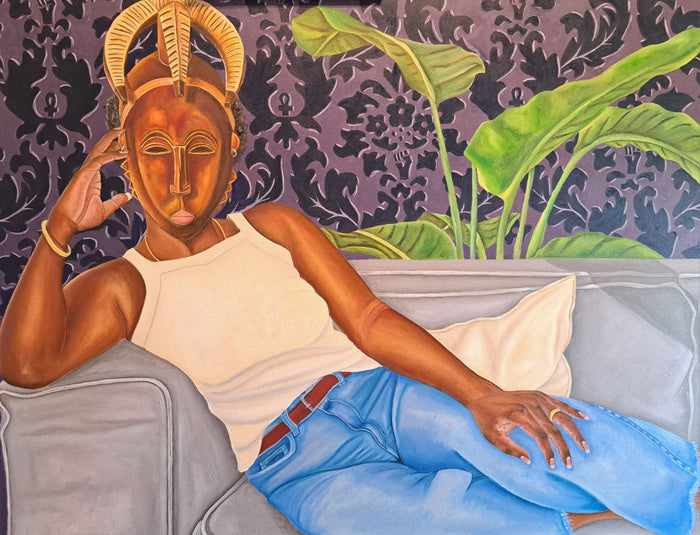 portrait of a woman of color in modern clothing lounging on a couch while wearing a traditional African mask; in the background there is a large leafy house plane and purple patterned wallpaper