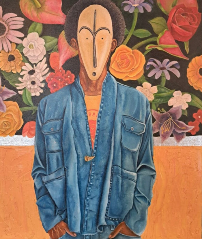 portrait of a man of color wearing a relaxed fit jean jacket and a traditional African mask; he stands in front of a floral façade handing over a concrete barrier wall 
