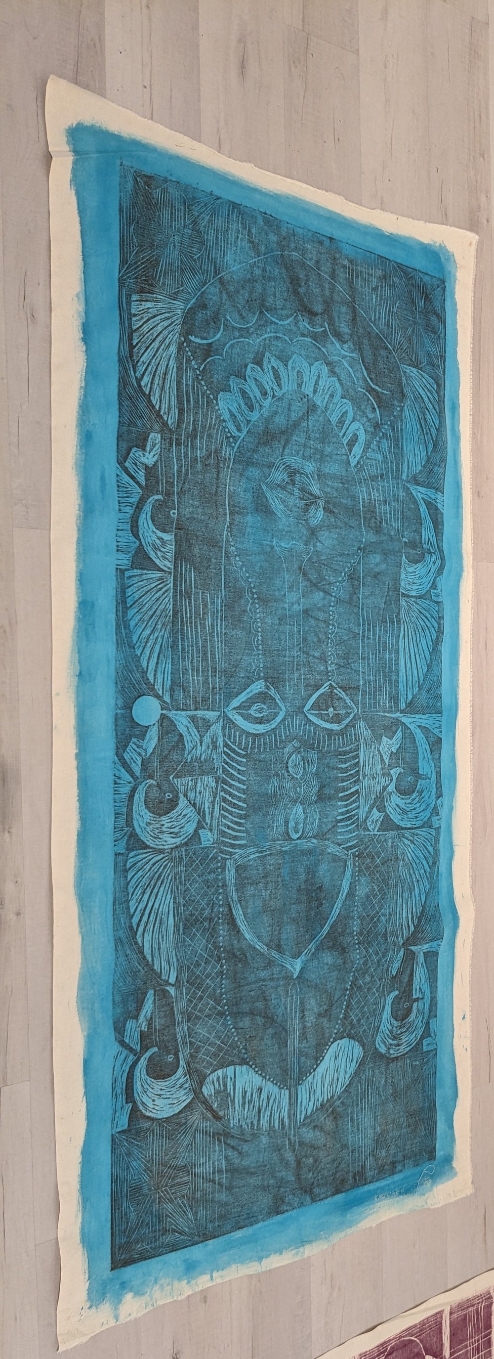 blue and black block print of an African mask on raw canvas