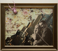 analog collage of a coup holding each other, one of which is on a landline phone with a cord; they stand in front of a sideways cityscape and a map with floral imagery on top of it; in the corner is a plastic deer with antlers