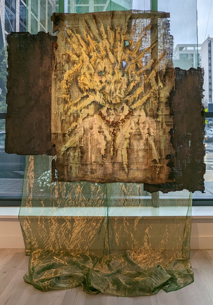 expressionistic painting on burlap featuring hues of green and brown with burnt and singe marks throughout; portrait hidden within painting