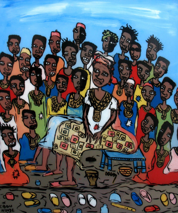 A group of African children being told a story by an african woman with their shoes all over the ground in front of them.  Multi colored.